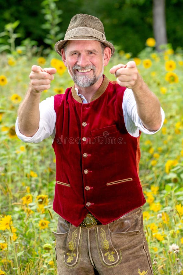 Un bel homme bavarois d'une cinquantaine d'années debout dans un jardin avec des pouces debout