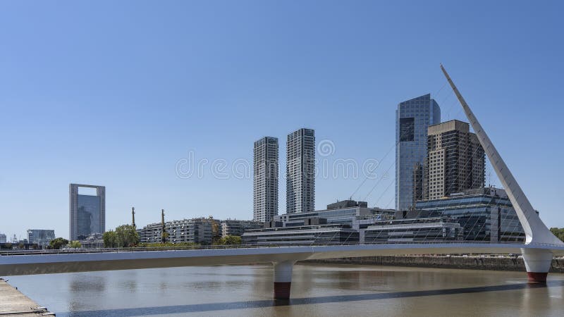 A beautiful pedestrian cable-stayed bridge Puente de la Mujer over the river. Stele and stretched metal strings against skyscrapers and city buildings. Clear blue sky. Argentina. Buenos Aires. A beautiful pedestrian cable-stayed bridge Puente de la Mujer over the river. Stele and stretched metal strings against skyscrapers and city buildings. Clear blue sky. Argentina. Buenos Aires.