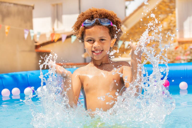 Un bel ragazzo spruzza l'acqua in una piccola piscina fotografia stock