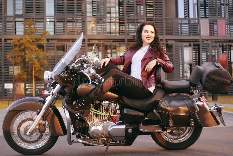 Un bello castana sta sedendosi su una bici vicino all'ufficio La ragazza è venuto a lavorare ad un motociclo Successo Ragazza Lez immagini stock Un bello castana sta sedendosi su una bici vicino all'ufficio La ragazza è venuto a lavorare ad un motociclo Successo Ragazza Lez immagini stock