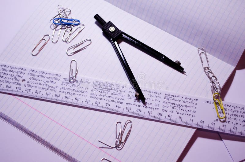 Un blocco appunti aperto con clip di carta, un righello e una bussola Apri notebook in una gabbia con accessori per la scuola Can immagini stock libere da diritti Un blocco appunti aperto con clip di carta, un righello e una bussola Apri notebook in una gabbia con accessori per la scuola Can immagini stock libere da diritti