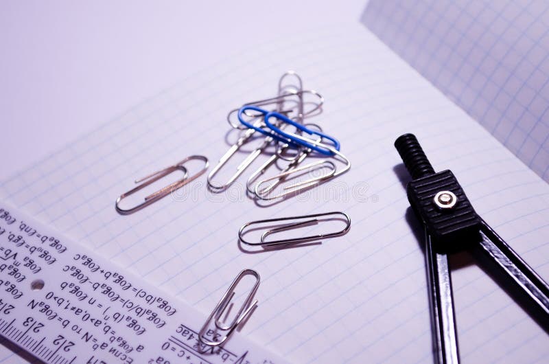 Un blocco appunti aperto con clip di carta, un righello e una bussola Apri notebook in una gabbia con accessori per la scuola Can fotografie stock Un blocco appunti aperto con clip di carta, un righello e una bussola Apri notebook in una gabbia con accessori per la scuola Can fotografie stock
