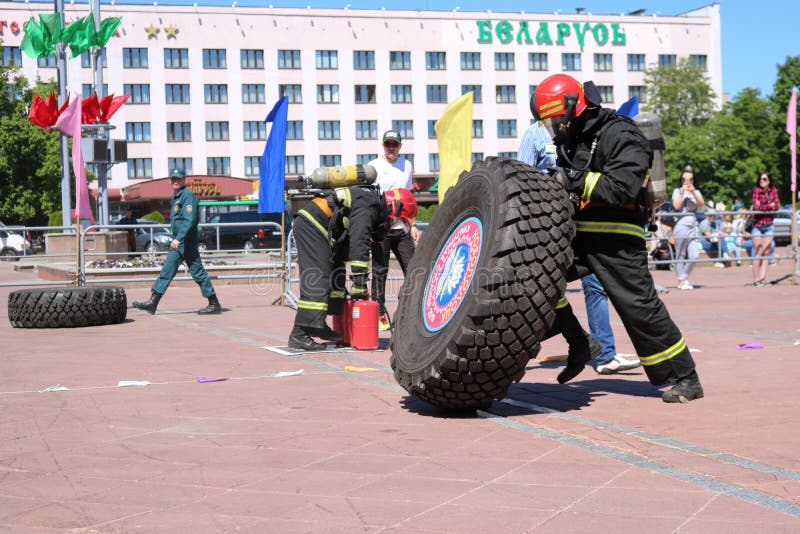 Un bombero en un traje incombustible corre y da vuelta a de goma grande rueda adentro una competencia de la lucha contra el fuego fotos de archivo libres de regalías