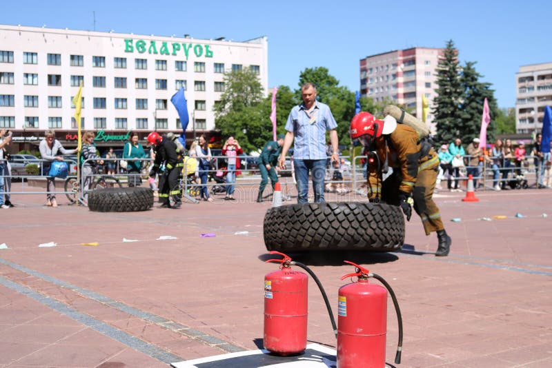 Un bombero en un traje incombustible corre y da vuelta a de goma grande rueda adentro una competencia de la lucha contra el fuego fotos de archivo