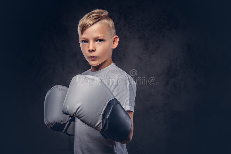 Un boxeur beau de petit garçon avec les cheveux blonds s'est habillé dans un T-shirt blanc dans les gants prêts à combattre D'iso image stock Un boxeur beau de petit garçon avec les cheveux blonds s'est habillé dans un T-shirt blanc dans les gants prêts à combattre D'iso image stock