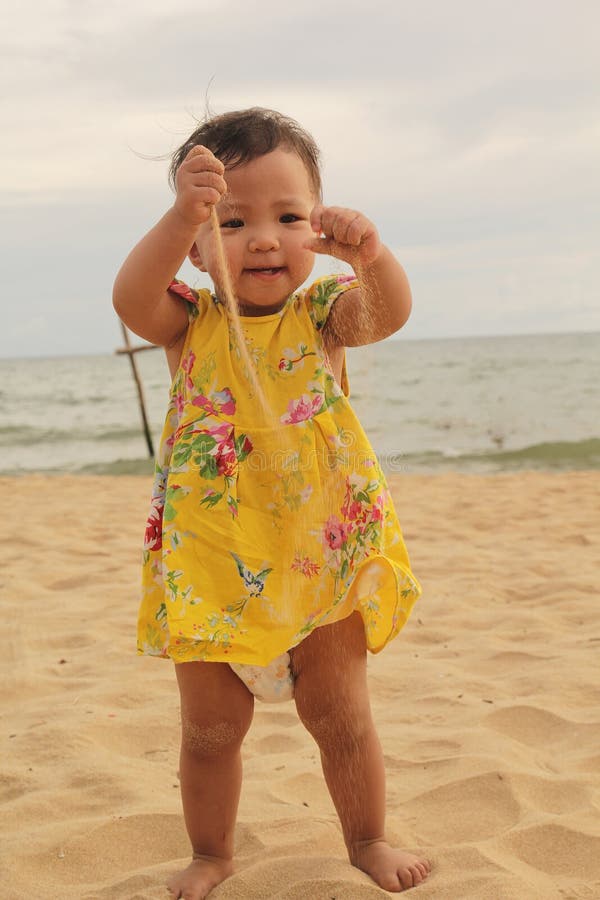 Un bébé est très heureux quand elle joue le sable sur la plage dans un jour d'été images libres de droits Un bébé est très heureux quand elle joue le sable sur la plage dans un jour d'été images libres de droits