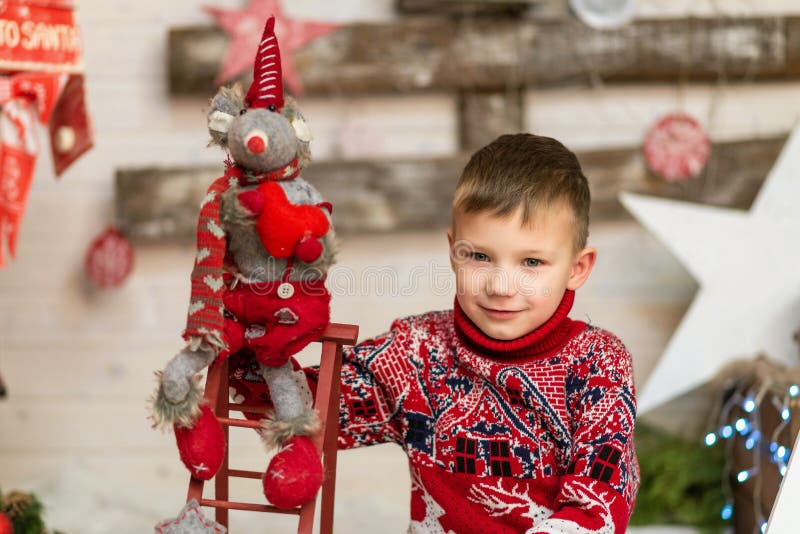 Un băiat în pulover roșu de Crăciun cu un simbol moale al unui șoarece de jucărie stock photos