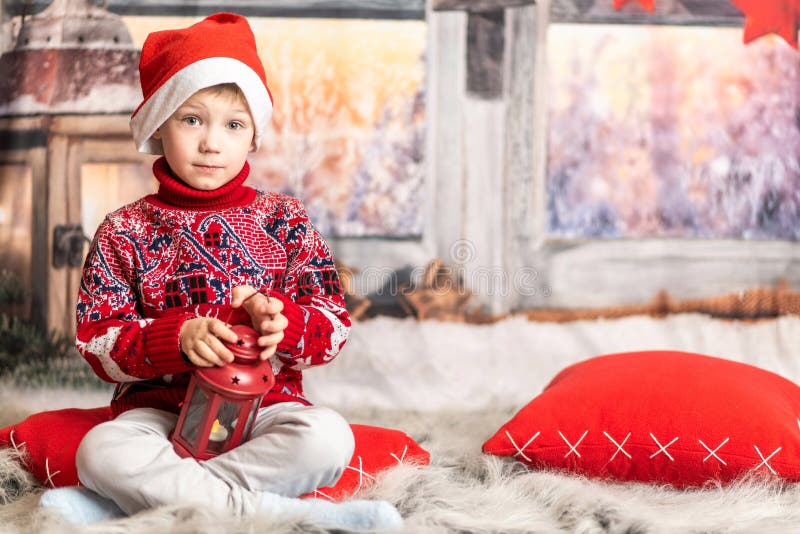 Un băiețel cu pălărie de Crăciun și un pulover roșu stă cu un felinar stock images