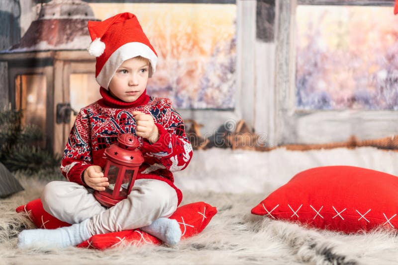 Un băiețel cu pălărie de Crăciun și un pulover roșu stă cu un felinar royalty free stock photos