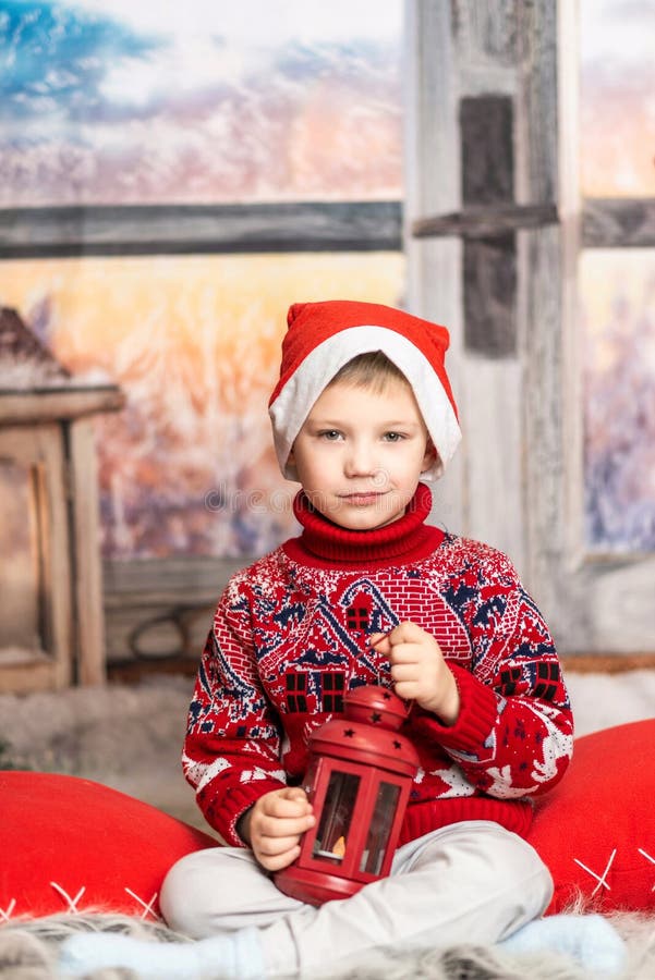 Un băiețel cu pălărie de Crăciun și un pulover roșu stă cu un felinar stock photo