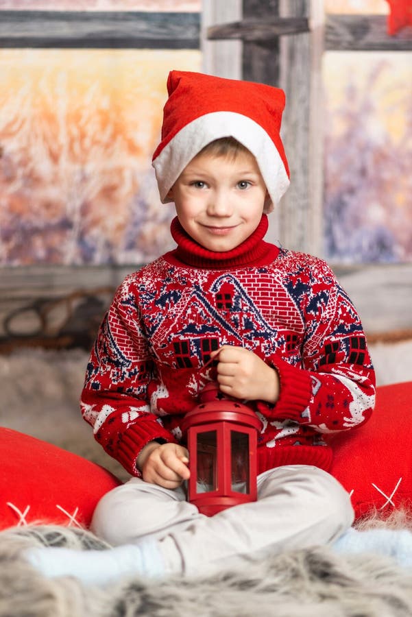 Un băiețel cu pălărie de Crăciun și un pulover roșu stă cu un felinar royalty free stock photo