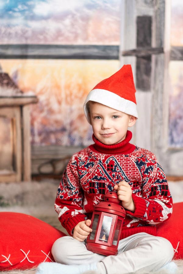 Un băiețel cu pălărie de Crăciun și un pulover roșu stă cu un felinar stock photos