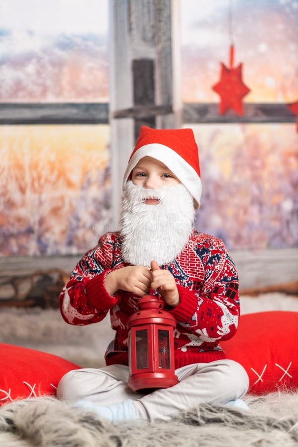 Un băiețel îmbrăcat ca un pitic de Crăciun cu o barbă care ține un felinar roșu royalty free stock photo