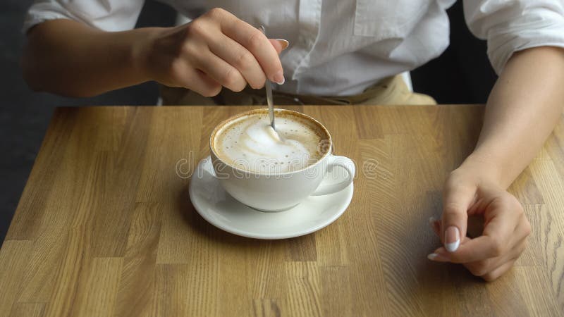 Un café de consumición de la mujer hermosa joven en un café Mano del azúcar stiring de la muchacha en cierre del café para arriba imagenes de archivo Un café de consumición de la mujer hermosa joven en un café Mano del azúcar stiring de la muchacha en cierre del café para arriba imagenes de archivo