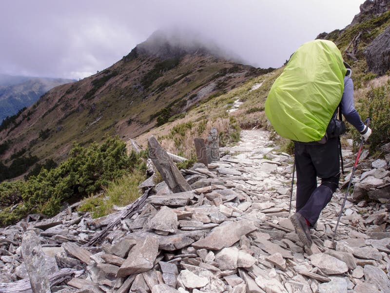 Un caminante masculino asiático que lleva una mochila grande con verdes fluorescentes, y caminando cuidadosamente en un rastro co imagen de archivo Un caminante masculino asiático que lleva una mochila grande con verdes fluorescentes, y caminando cuidadosamente en un rastro co imagen de archivo