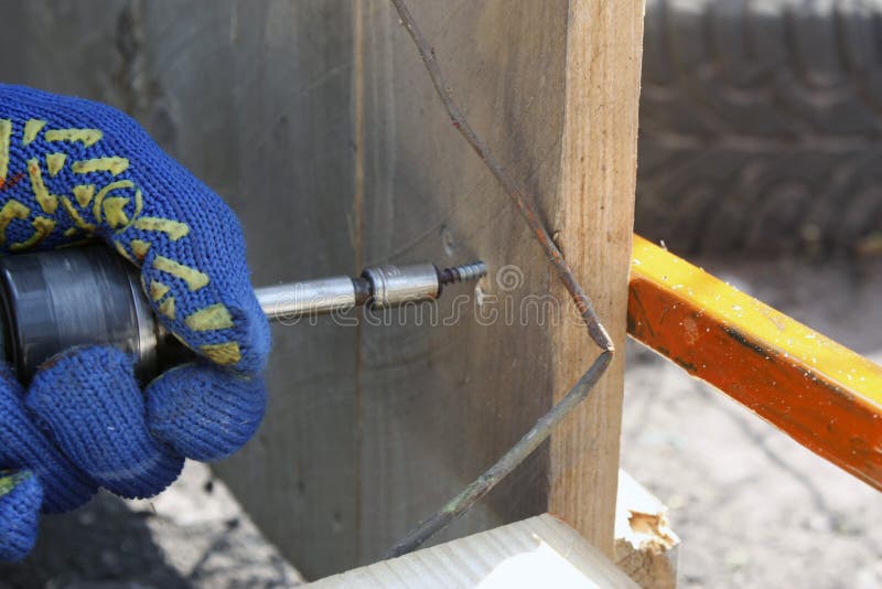 Un carpintero que trabaja con un destornillador eléctrico que repara una cerca de madera en guantes protectores imagen de archivo Un carpintero que trabaja con un destornillador eléctrico que repara una cerca de madera en guantes protectores imagen de archivo