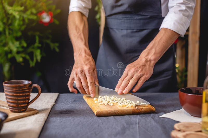 Un chef de un delantal negro prepara un plato navideño cortando ajo Cocina alegre para la mesa festiva de año nuevo imagen de archivo