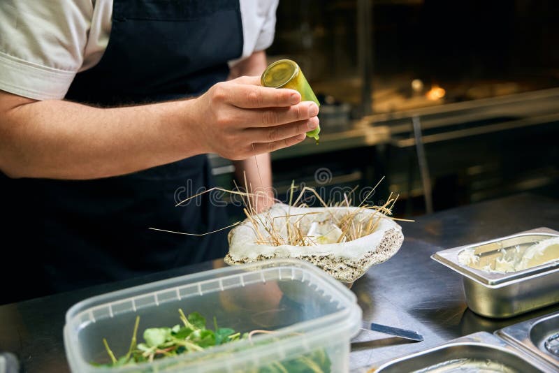 Un chef varón parcial vertiendo aceite o especias en ostras en el plato del nido en el restaurante fotografía de archivo