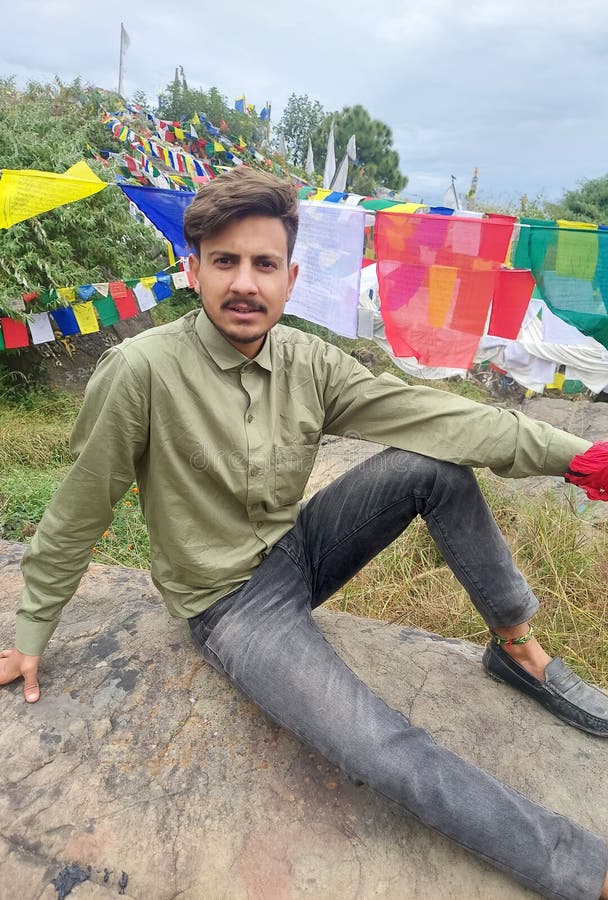 Un chico guapo mirando la cámara mientras se sienta en la roca con el fondo de banderas de oración tibetana en rewalsar.