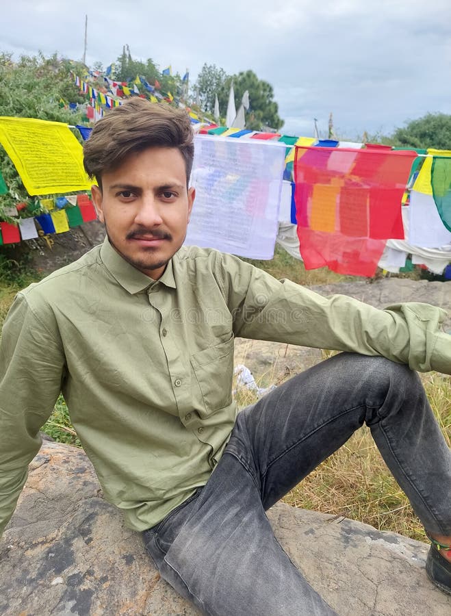 Un chico guapo mirando la cámara mientras se sienta en la roca con el fondo de banderas de oración tibetana en rewalsar fotos de archivo libres de regalías
