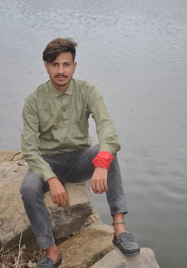 Un chico joven mirando una cámara sentado en piedra junto al lago imagen de archivo libre de regalías