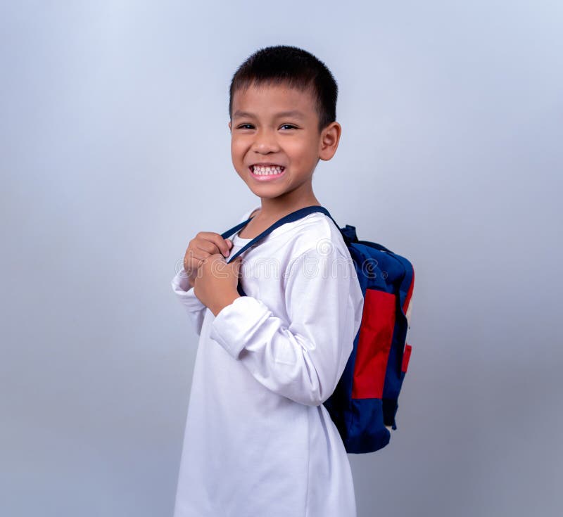 Un chico lindo asiático vestido de blanco y con mochila estudiantil parado en el estilo de vida de un chico con un blanco fotografía de archivo libre de regalías