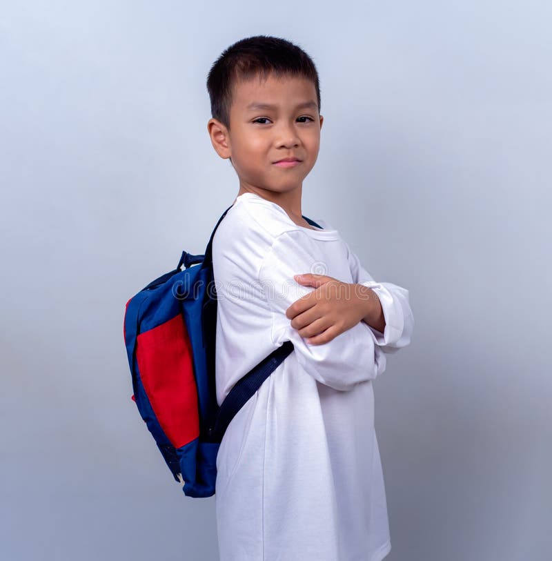 Un chico lindo asiático vestido de blanco y con mochila estudiantil parado en el estilo de vida de un chico con un blanco fotos de archivo