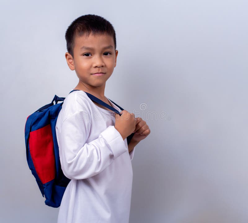 Un chico lindo asiático vestido de blanco y con mochila estudiantil parado en el estilo de vida de un chico con un blanco fotos de archivo