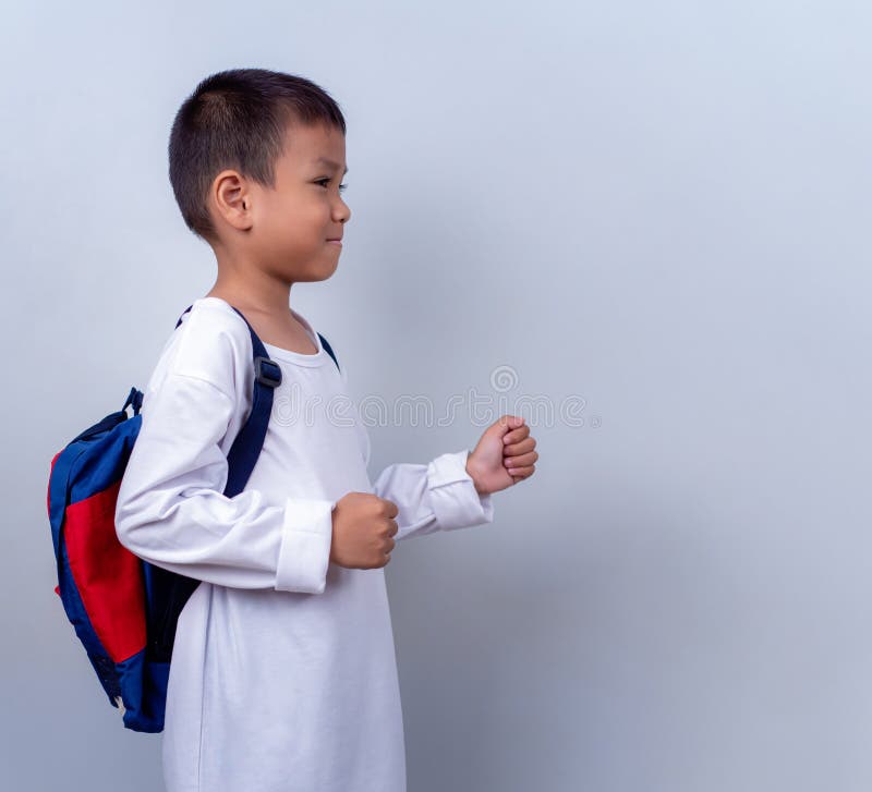 Un chico lindo asiático vestido de blanco y con mochila estudiantil parado en el estilo de vida de un chico con un blanco imagen de archivo libre de regalías