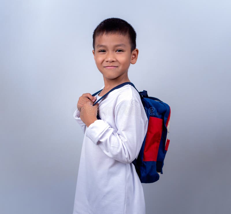 Un chico lindo asiático vestido de blanco y con mochila estudiantil parado en el estilo de vida de un chico con un blanco foto de archivo libre de regalías