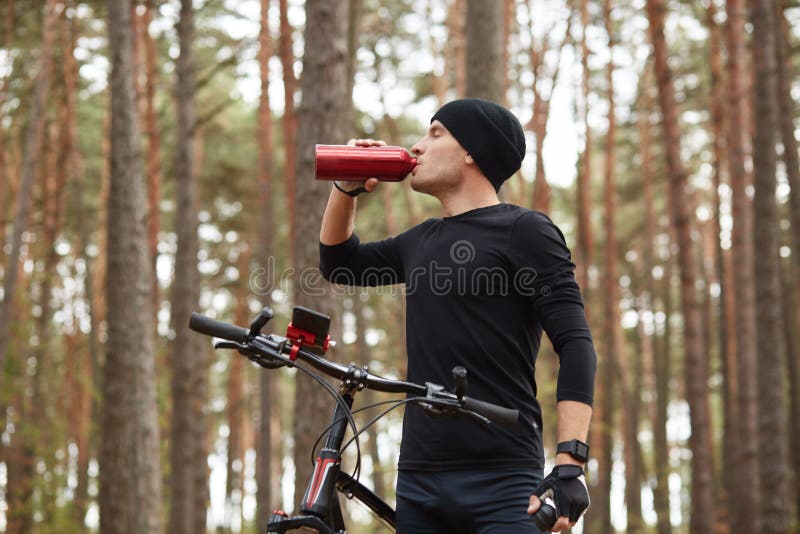 Un Ciclista Vestido Traje Deportivo Negro Y Gorra Parado Cerca De Su Bicicleta, Tomando Agua De Una Botella Deportiva Imagen de archivo - Imagen de rotura, muchacho: 159755509