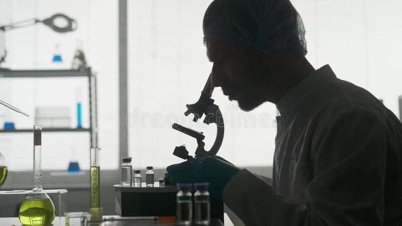 Un científico de un laboratorio de investigación examina una muestra de un micropreparado utilizando un microscopio. la silueta os metrajes