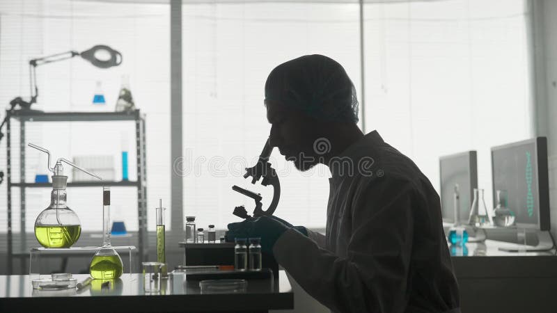 Un científico de un laboratorio de investigación examina una muestra de un micropreparado utilizando un microscopio. vista lateral almacen de metraje de vídeo