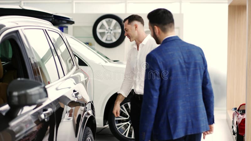 Un cliente masculino que elige un coche en el concesionario con la ayuda de un vendedor automático en cámara lenta almacen de metraje de vídeo