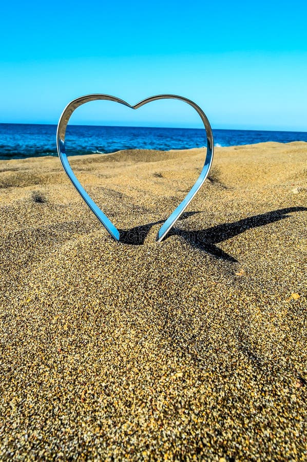 A heart made of metal is on the beach. The heart is surrounded by sand and the ocean. The scene is peaceful and serene. A heart made of metal is on the beach. The heart is surrounded by sand and the ocean. The scene is peaceful and serene