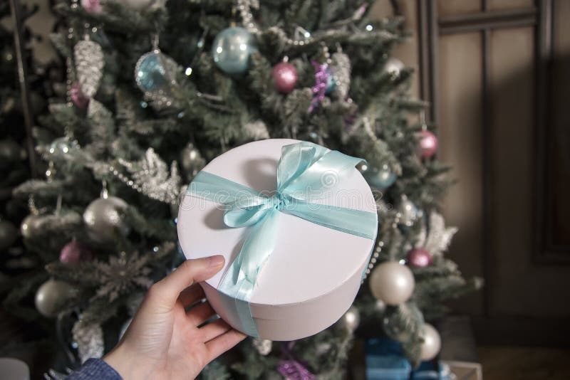 In un contenitore bianco di mano con un regalo La ragazza con un regalo L'abete di un nuovo anno contro lo sfondo di fotografia stock In un contenitore bianco di mano con un regalo La ragazza con un regalo L'abete di un nuovo anno contro lo sfondo di fotografia stock