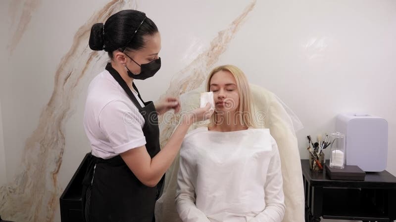 Un cosmetologo pulisce le sopracciglia con tamponi di cotone dopo un trucco permanente. video d archivio