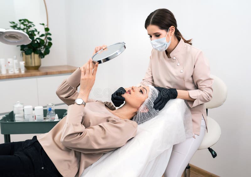 Un cosmétologue ou un dermatologue fait un traitement de spa au patient avec un miroir dans l'armoire de cosmétologie image stock