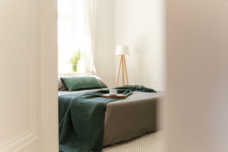 Un coup d'oeil par une porte ouverte sur un lit s'est habillé dans la toile grise et verte, des oreillers et une couverture dans images stock Un coup d'oeil par une porte ouverte sur un lit s'est habillé dans la toile grise et verte, des oreillers et une couverture dans images stock
