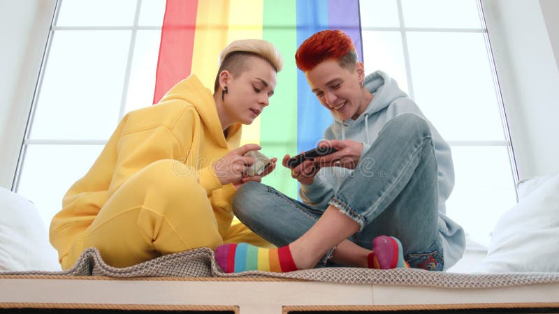 Un couple avec un drapeau arc-en-ciel et des smartphones montrant l'amour et l'unité dans un cadre cosy banque de vidéos