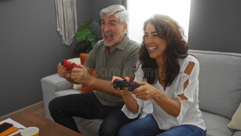 Un couple d'âge moyen qui s'amuse à jouer ensemble sur un canapé dans leur salon confortable images stock