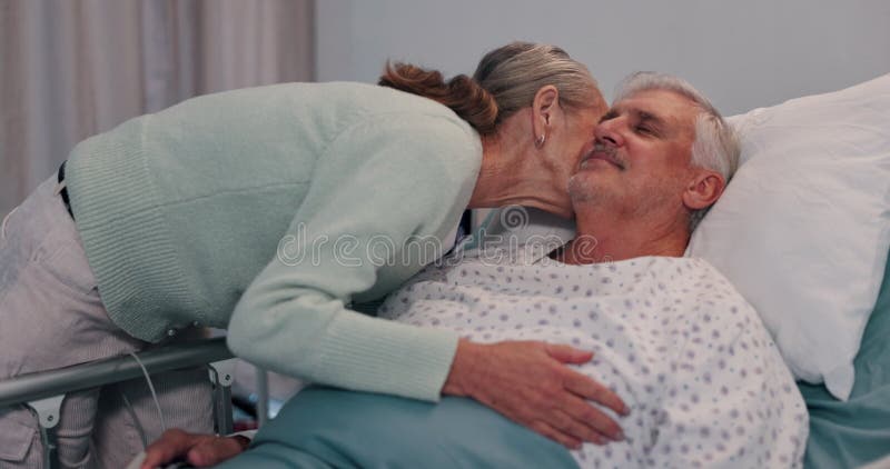 Un couple et un baiser à l'hôpital pour l'affection et les soins du vieil homme sur le lit câlin ou soutien. Soins de santé banque de vidéos