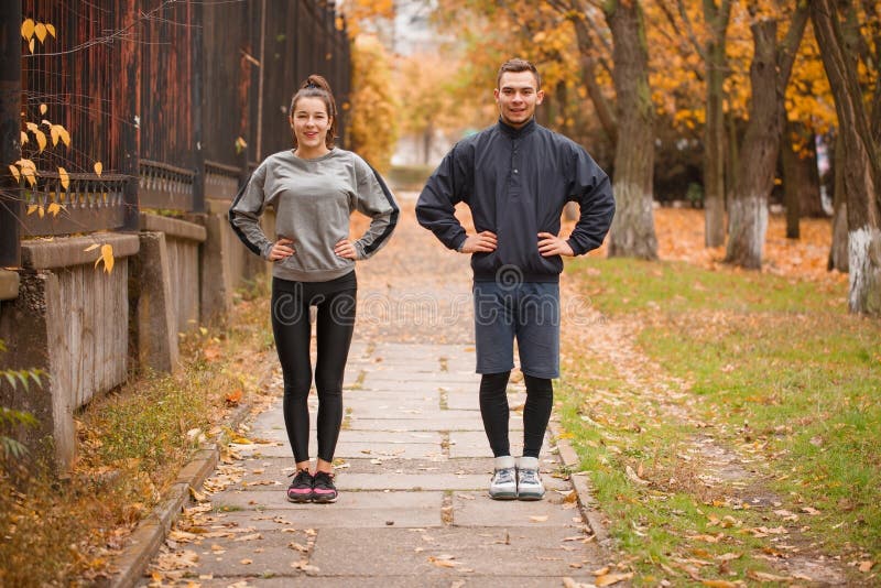 Un couple fait des sports en parc d'automne Position avec vos mains sur votre taille photographie stock libre de droits Un couple fait des sports en parc d'automne Position avec vos mains sur votre taille photographie stock libre de droits
