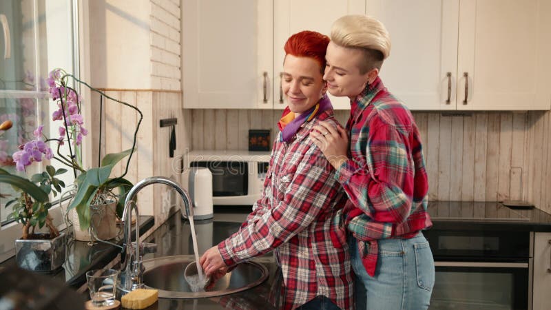 Un couple fait joyeusement les corvées ensemble dans leur cuisine chaude en profitant de la lumière du soleil et des tâches partag banque de vidéos