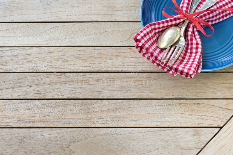 A Red White and Blue Picnic Table Place Setting with napkin, fork and spoon and plate in an upper corner on horizontal wood board table top background with room or space for copy, text or your words. A Red White and Blue Picnic Table Place Setting with napkin, fork and spoon and plate in an upper corner on horizontal wood board table top background with room or space for copy, text or your words.