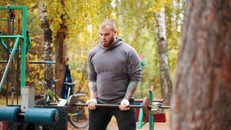Un culturiste tatoué se pompant les mains avec la cloche derrière le dos - s'entrainant sur le terrain de sport extérieur photographie stock libre de droits Un culturiste tatoué se pompant les mains avec la cloche derrière le dos - s'entrainant sur le terrain de sport extérieur photographie stock libre de droits
