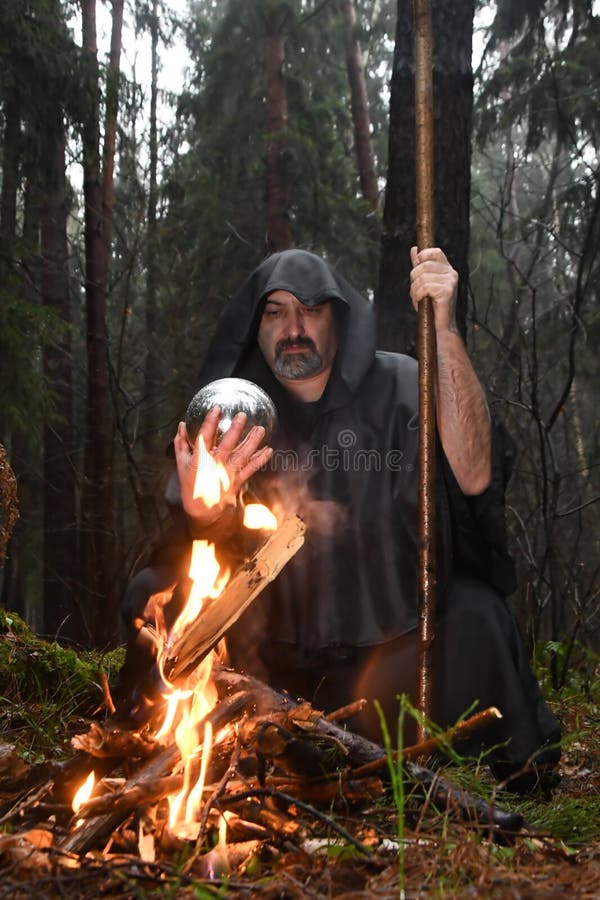 Un călugăr șantajat stă lângă un foc în pădure și se uită într-o minge de divinație. misticism și vrăjitori magici și vrăjitori 3 stock photos