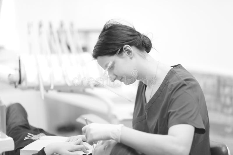 Un dentista de sexo femenino examina la cavidad bucal de un paciente imagen de archivo Un dentista de sexo femenino examina la cavidad bucal de un paciente imagen de archivo