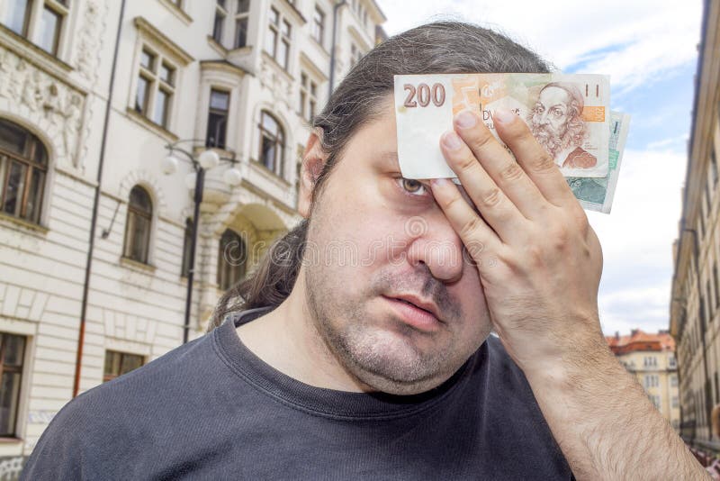 Un disgustado hombre adulto de mediana edad con pelo largo de cola de caballo sostiene varios billetes checos de corona