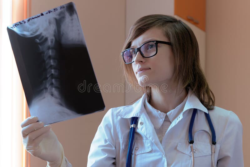 Un doctor joven en un vestido médico con vidrios y un estetoscopio en sus miradas del cuello de cerca en la radiografía fotografía de archivo Un doctor joven en un vestido médico con vidrios y un estetoscopio en sus miradas del cuello de cerca en la radiografía fotografía de archivo